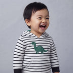 Bebé riendo feliz con buzo EmpiBy de rayas blancas y negras con estampado de dinosaurio verde en el pecho