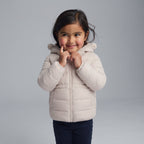 Niña sonriente vistiendo chaqueta acolchada beige con capucha de osito de la marca EmpiBy