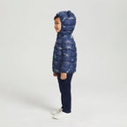 Niño sonriente vistiendo chaqueta acolchada EmpiBy azul marino con estampado de esqueletos de dinosaurios y capucha