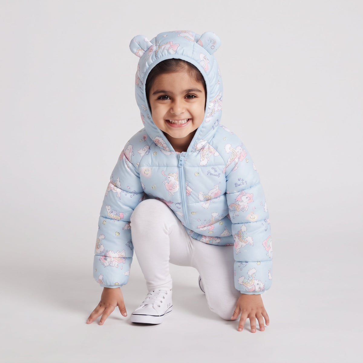 Niña sonriente con chaqueta acolchada EmpiBy azul claro con estampado de unicornios y capucha con orejas