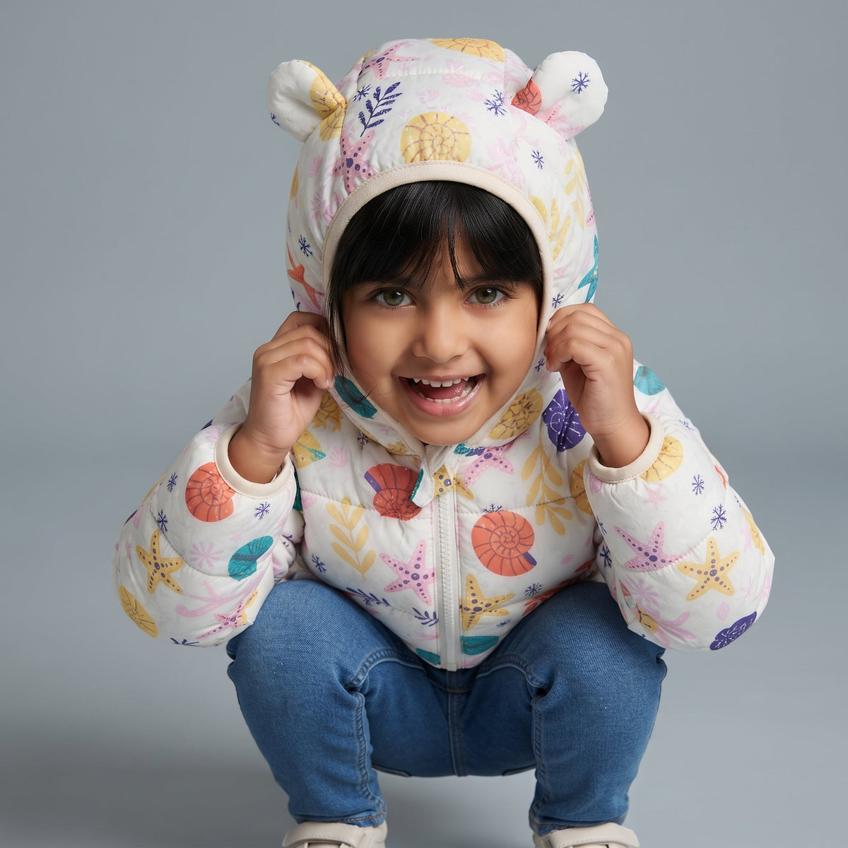 Niña sonriente usando chaqueta EmpiBy acolchada con estampado de motivos marinos y capucha con orejitas