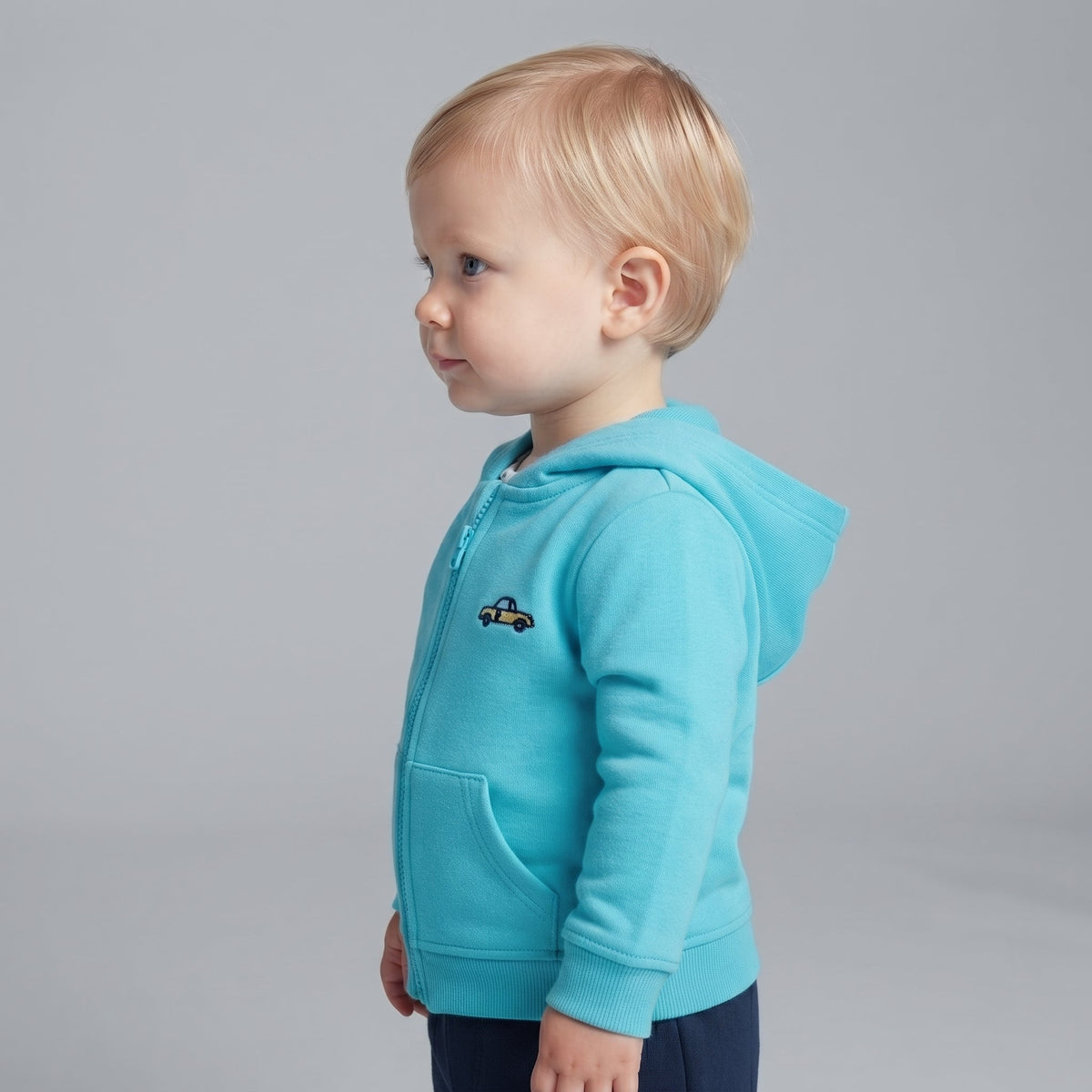 Niño pequeño vistiendo chaqueta EmpiBy azul turquesa con capucha y bordado de coche amarillo, vista de perfil