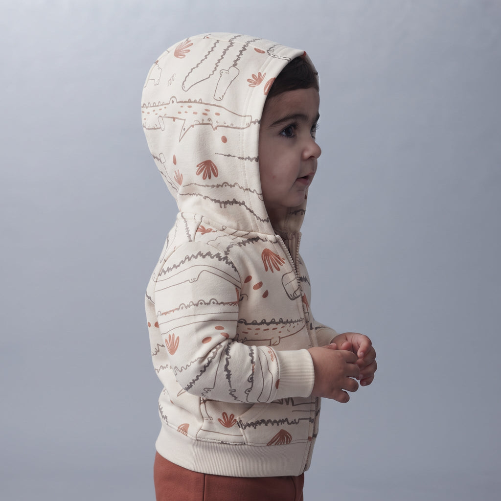 Bebé con chaqueta beige con capucha y estampado de cocodrilos de EmpiBy, vista lateral, estilo casual y cómodo.