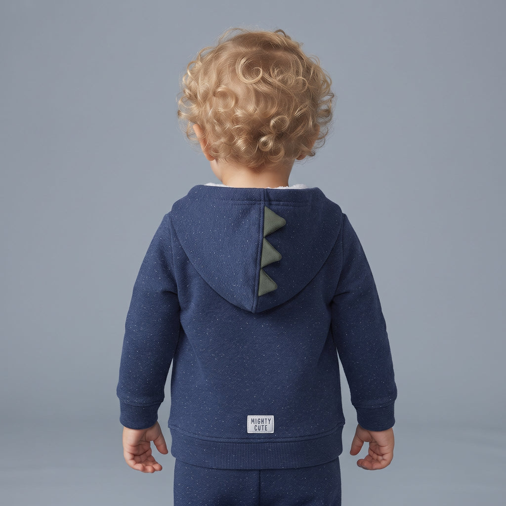 Bebé de espaldas vistiendo chaqueta azul EmpiBy con capucha y cresta de dinosaurio verde, estilo prehistórico.