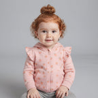 Bebé niña con pelo rizado pelirrojo vistiendo chaqueta rosa con estampado de melocotones de EmpiBy