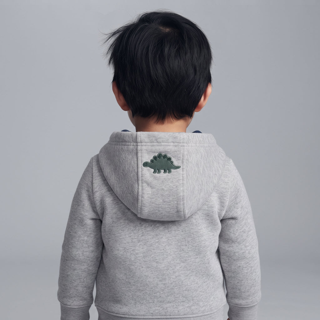 Niño de espaldas vistiendo una chaqueta gris con capucha de EmpiBy que tiene un dinosaurio bordado en la parte trasera