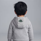 Niño de espaldas vistiendo una chaqueta gris con capucha de EmpiBy que tiene un dinosaurio bordado en la parte trasera