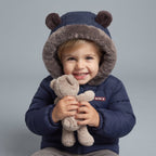 Niño sonriente con chaqueta azul EmpiBy con capucha de osito y forro de piel sintética abrazando un peluche