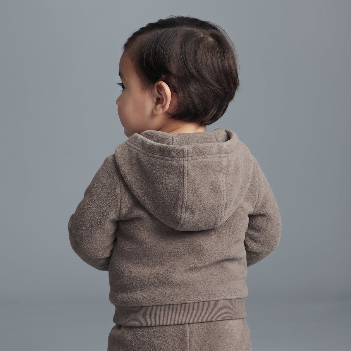 Bebé de espaldas vistiendo chaqueta polar marrón topo con capucha de EmpiBy, suave y abrigada para el invierno.