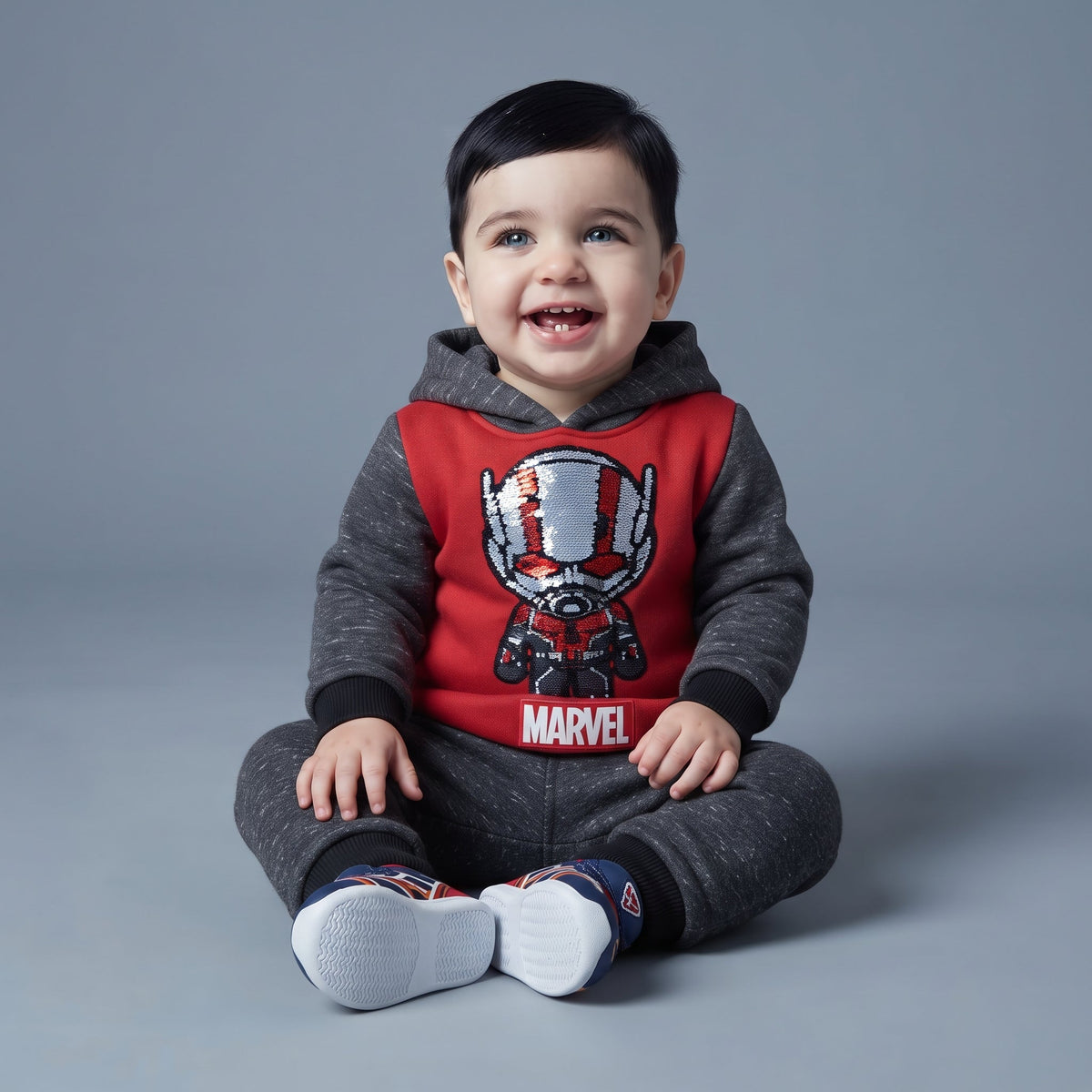 Bebé sonriente vistiendo conjunto EmpiBy de dos piezas de Ant-Man en gris melange y rojo con detalles de lentejuelas.