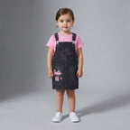 Niña pequeña vistiendo conjunto EmpiBy de Barbie con vestido jardinera de mezclilla oscuro y camiseta rosa estampada