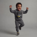 Bebé feliz saltando con conjunto EmpiBy de sudadera y jogger gris de Batman con detalles en amarillo y negro