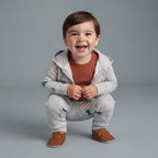 Bebé sonriente con conjunto EmpiBy de 3 piezas: chaqueta y pantalón gris con animales del bosque y body terracota.