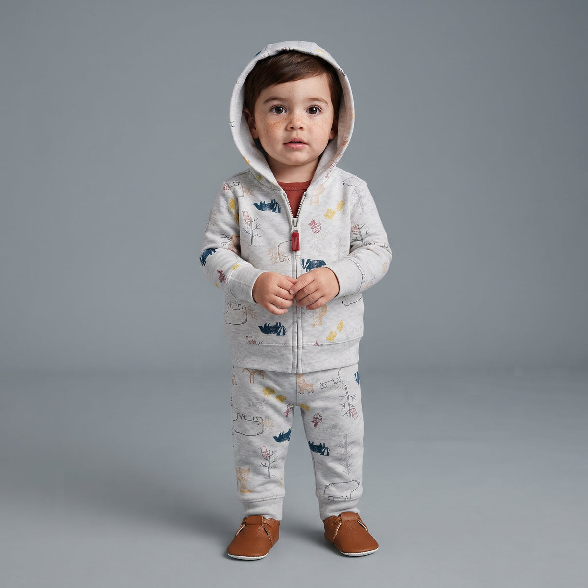 Bebé con conjunto EmpiBy de 3 piezas: chaqueta con capucha gris, pantalón estampado de animales y body terracota.