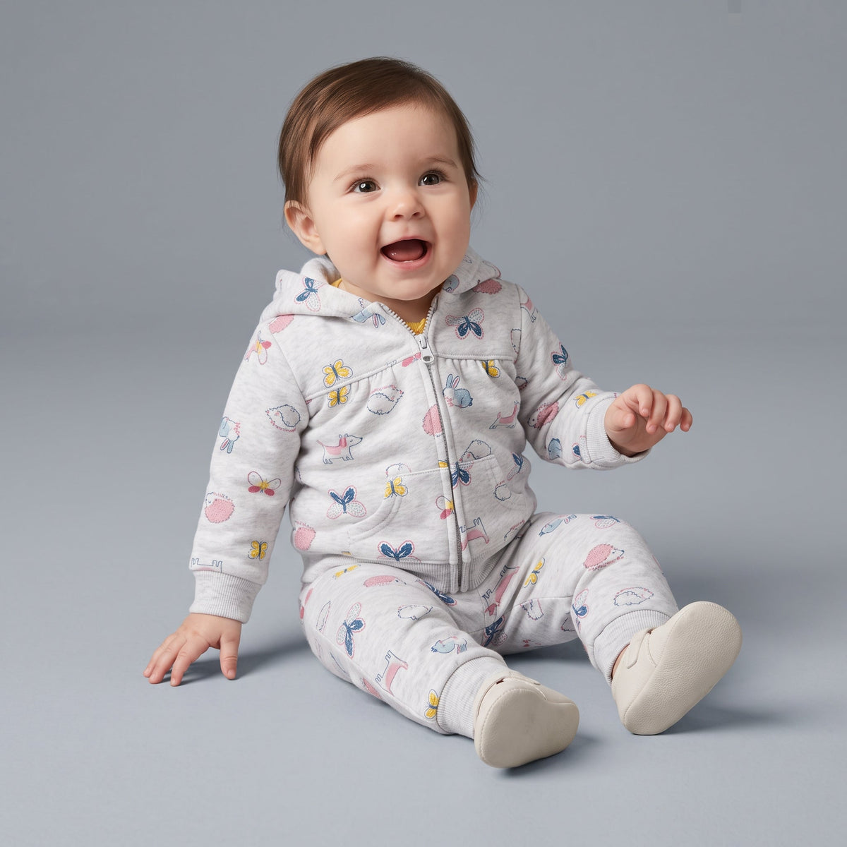 Bebé feliz vistiendo conjunto EmpiBy de tres piezas gris con estampado de animalitos, chaqueta con capucha y jogger