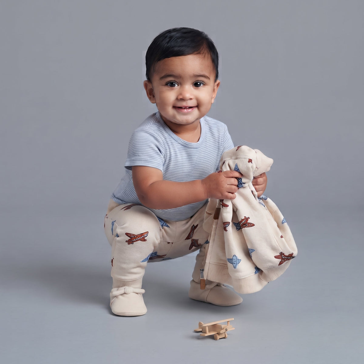 Bebé sonriente con conjunto EmpiBy de 3 piezas: body a rayas, pantalón y chaqueta con estampado de aviones.