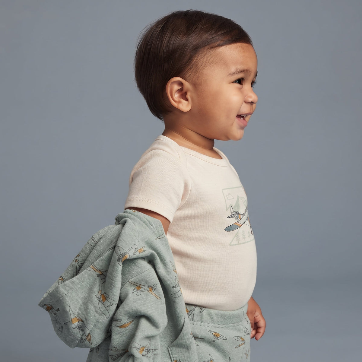 Bebé con conjunto de 3 piezas EmpiBy, body beige con estampado de avión y chaqueta verde salvia con avionetas.