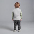 Vista trasera de niño pequeño con conjunto EmpiBy: chaleco acolchado gris, body verde a rayas y pantalón estampado.