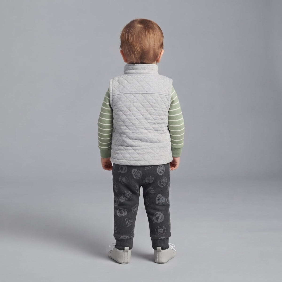 Vista trasera de niño pequeño con conjunto EmpiBy: chaleco acolchado gris, body verde a rayas y pantalón estampado.