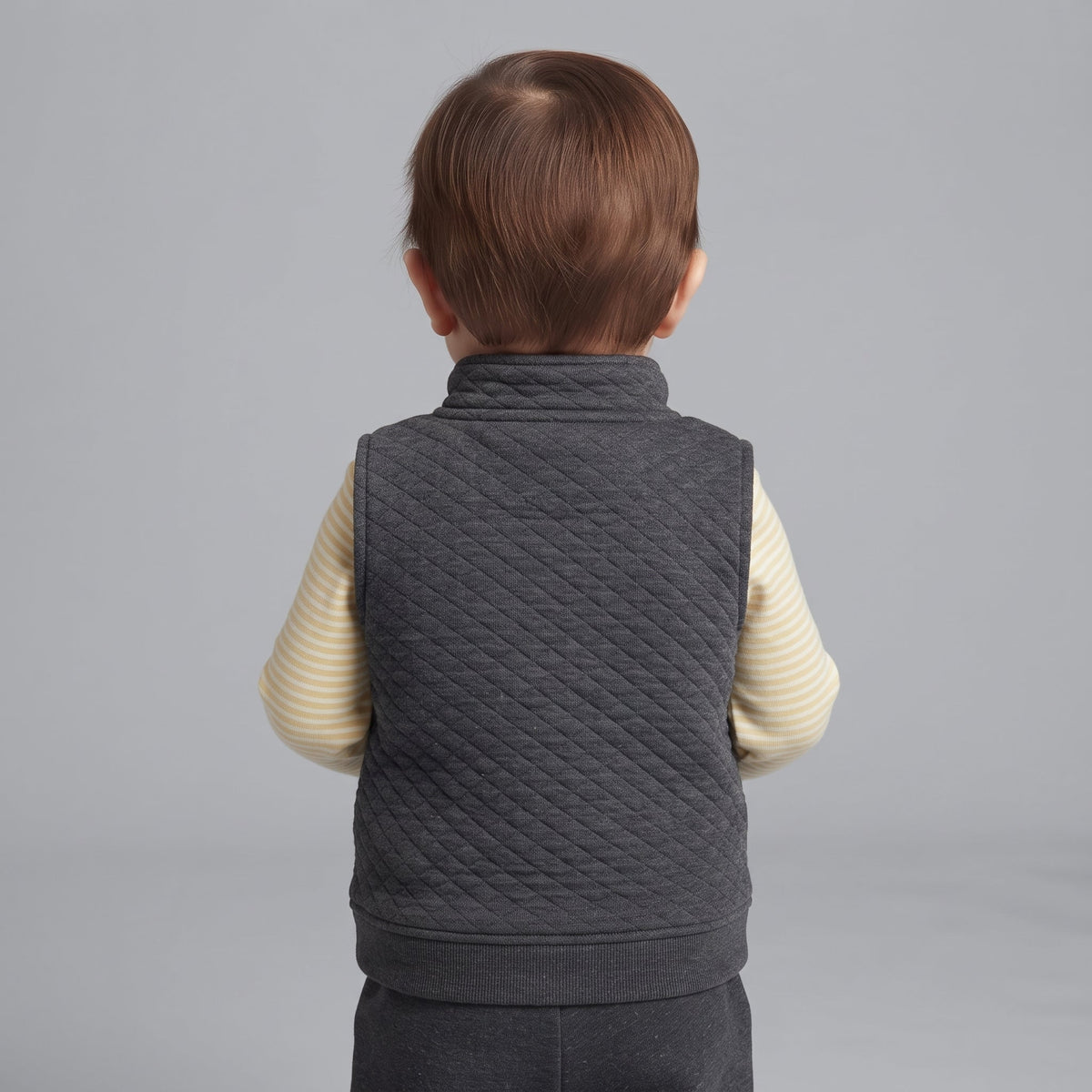 Vista trasera de bebé niño con conjunto EmpiBy de chaleco acolchado gris oscuro y body de rayas amarillas