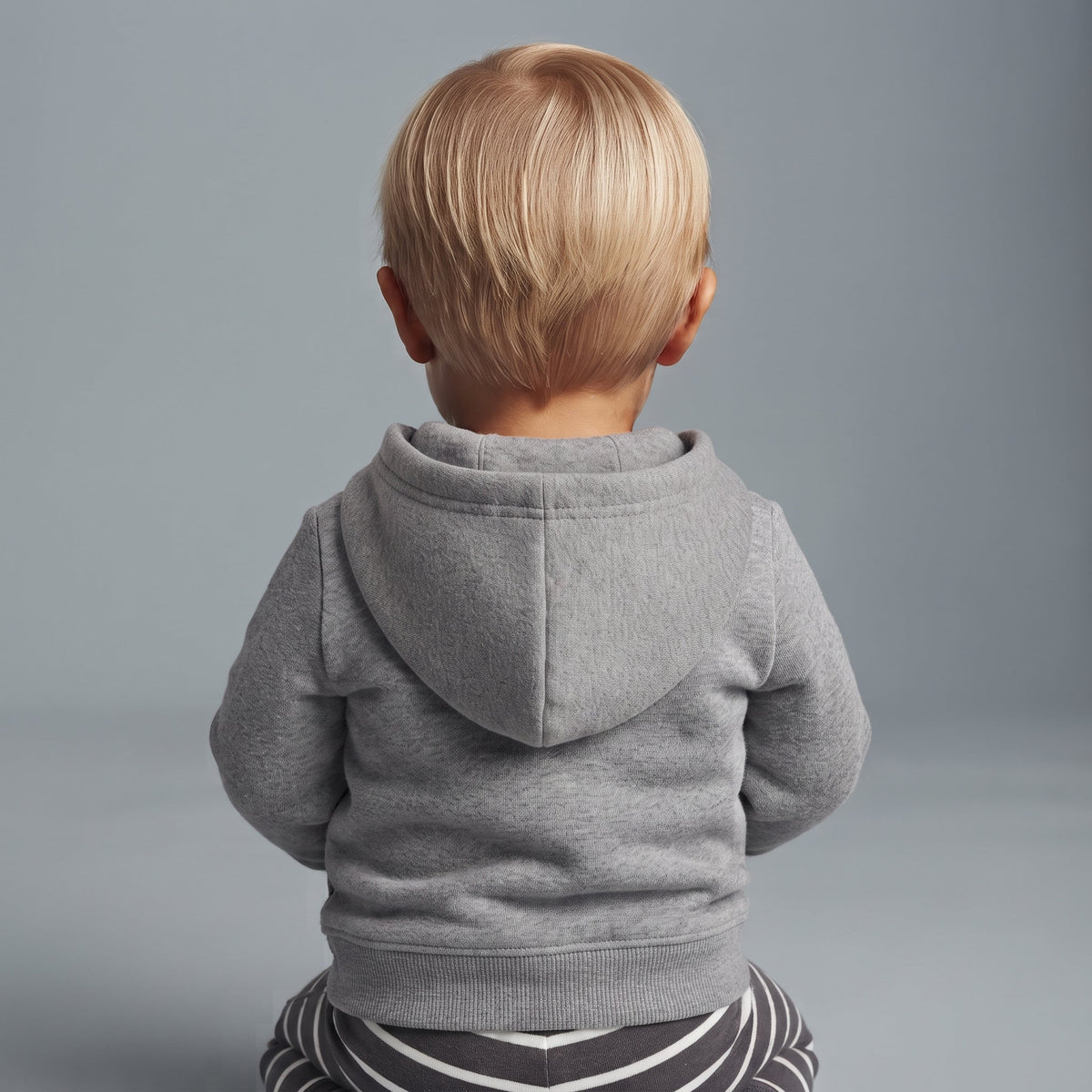 Bebé de espaldas vistiendo chaqueta hoodie gris de EmpiBy con pantalón de rayas sobre fondo neutro