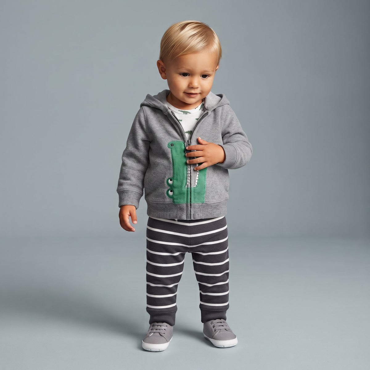Bebé con conjunto EmpiBy de 3 piezas: chaqueta gris con cocodrilo, body estampado y pantalón a rayas grises y blancas.