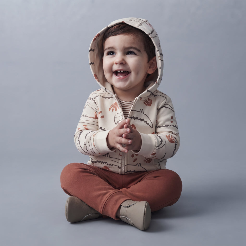 Bebé sonriente con conjunto EmpiBy de 3 piezas: chaqueta beige con cocodrilos, body a rayas y pantalón marrón.