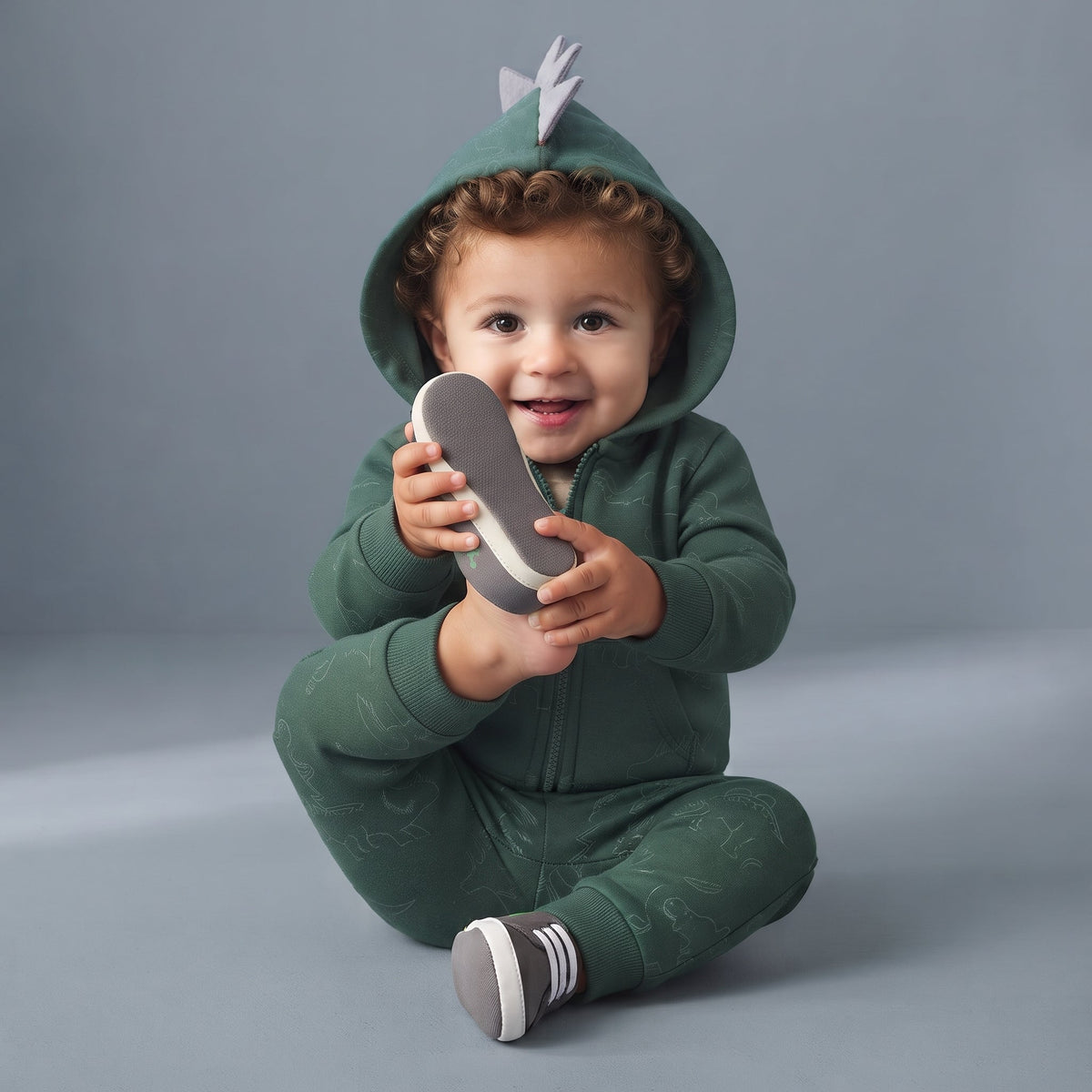 Bebé sonriente con conjunto EmpiBy de 3 piezas verde bosque, chaqueta con capucha de dinosaurio y estampado de T-Rex.