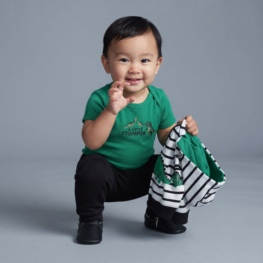 Bebé sonriente con conjunto EmpiBy de body verde, pantalón negro y chaqueta a rayas con estampado de dinosaurio