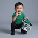 Bebé sonriente con conjunto EmpiBy de body verde, pantalón negro y chaqueta a rayas con estampado de dinosaurio