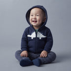 Bebé sonriente con conjunto EmpiBy de 3 piezas: chaqueta azul con dinosaurio, body verde y pantalón de rayas.