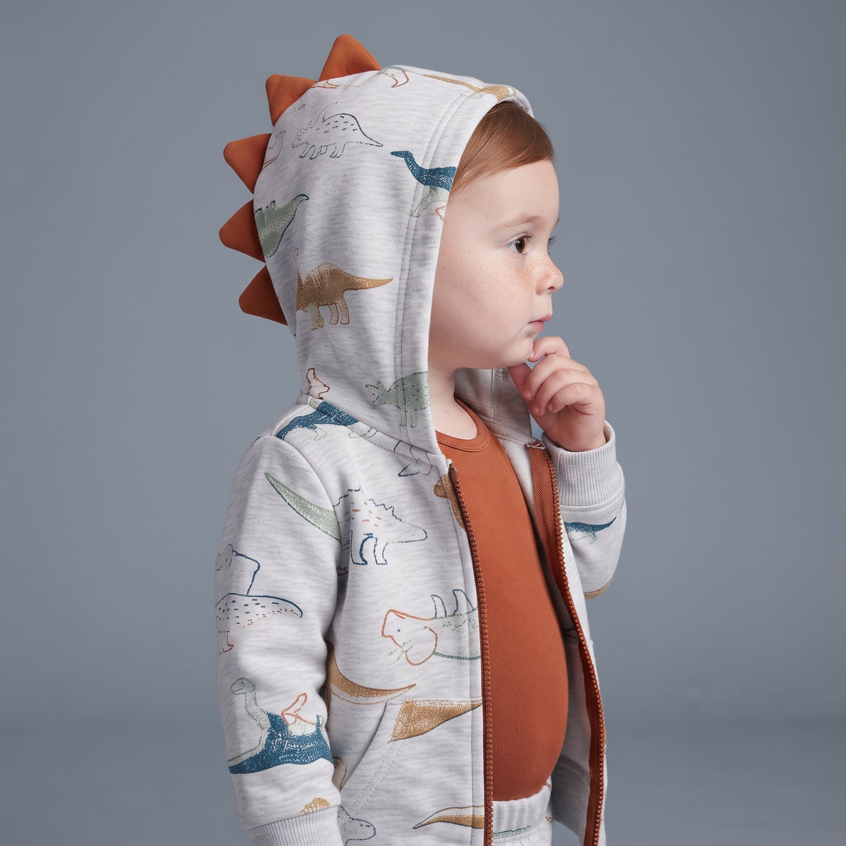 Bebé con conjunto EmpiBy de 3 piezas: chaqueta gris con capucha de dinosaurio, body terracota y pantalón estampado