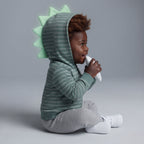 Bebé con conjunto EmpiBy de 3 piezas: chaqueta a rayas verde con capucha de dinosaurio, body blanco y pantalón gris.