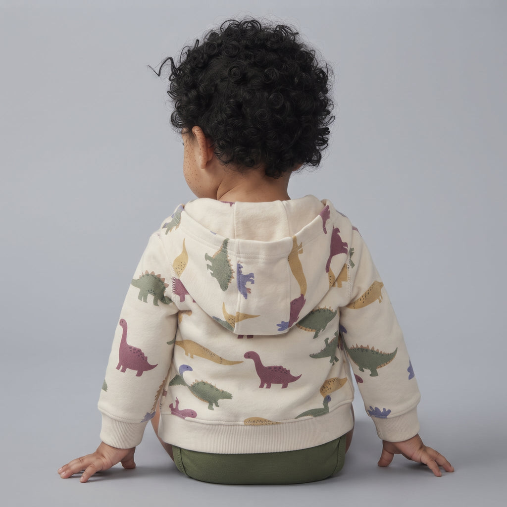 Bebé de espaldas vistiendo chaqueta beige con capucha y estampado de dinosaurios de la marca EmpiBy