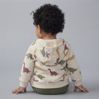 Bebé de espaldas vistiendo chaqueta beige con capucha y estampado de dinosaurios de la marca EmpiBy