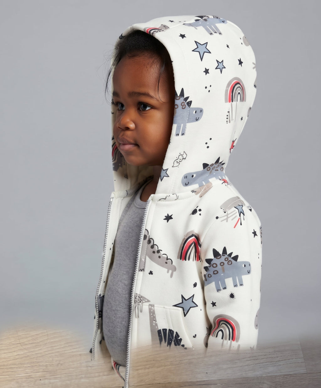 Niño pequeño con conjunto EmpiBy de chaqueta blanca con estampado de dinosaurios, arcoíris y estrellas con capucha.