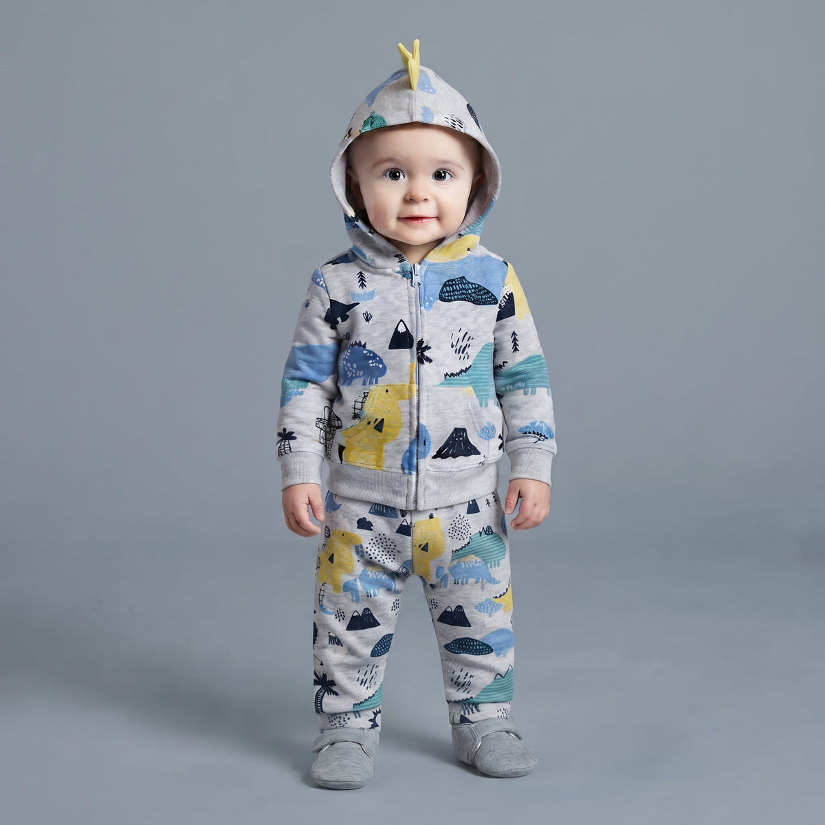 Bebé con conjunto EmpiBy de tres piezas gris con estampado de dinosaurios, chaqueta con capucha y pantalón a juego.