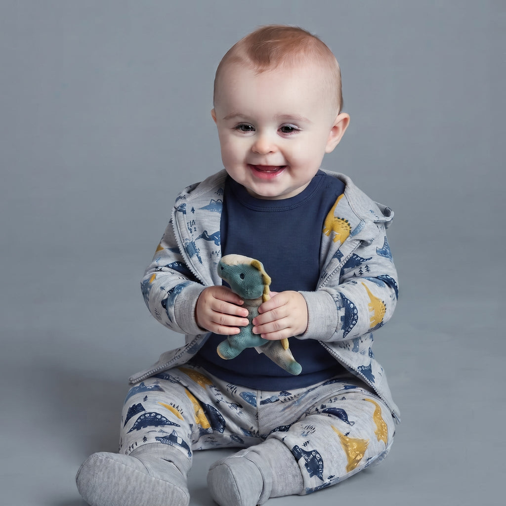 Bebé sonriente con conjunto EmpiBy de tres piezas con estampado de dinosaurios, chaqueta gris y body azul oscuro.