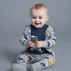 Bebé sonriente con conjunto EmpiBy de tres piezas con estampado de dinosaurios, chaqueta gris y body azul oscuro.