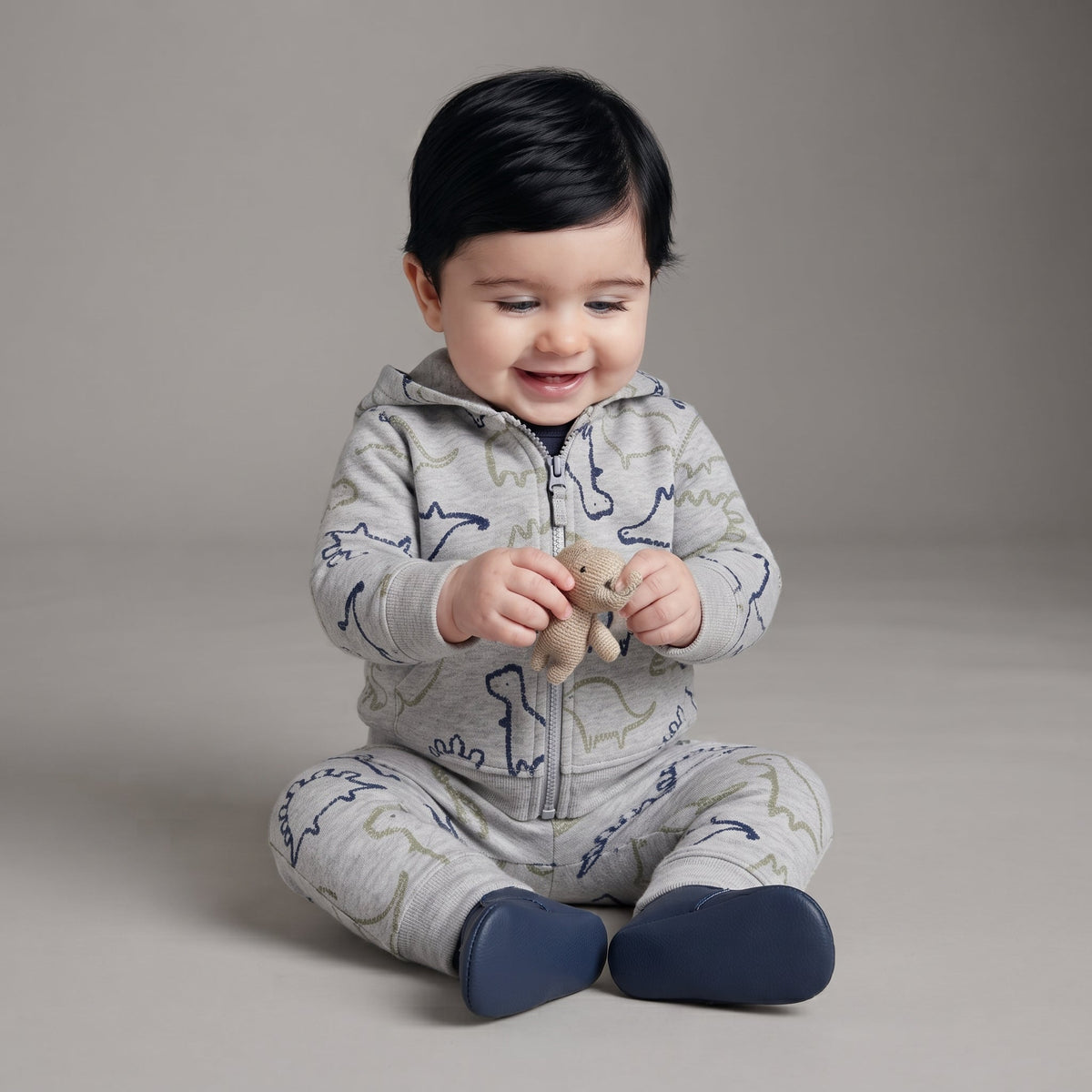 Bebé sonriente con conjunto EmpiBy de tres piezas gris con estampado de dinosaurios, chaqueta con capucha y body