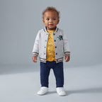 Bebé con conjunto EmpiBy de 3 piezas: chaqueta bomber gris, body amarillo de dinosaurios y pantalón azul marino.