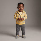 Bebé con conjunto EmpiBy de 3 piezas: chaqueta amarilla con dinosaurios, body a rayas y pantalón gris cómodo.