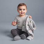 Bebé sonriente con conjunto EmpiBy de 3 piezas: body a rayas, pantalón gris y chaqueta con estampado de dinosaurios.