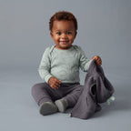 Bebé sonriente con conjunto EmpiBy de body verde con dinosaurios, pantalón gris y chaleco con capucha de picos