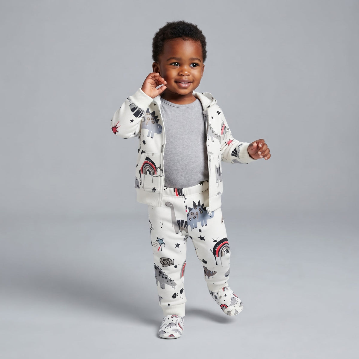 Bebé sonriente vistiendo conjunto EmpiBy de 3 piezas con estampado de dinosaurios, chaqueta blanca y body gris