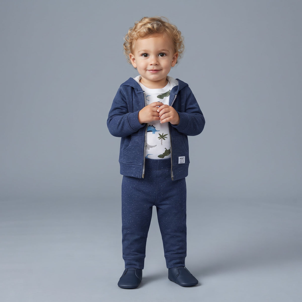 Niño pequeño con conjunto EmpiBy de tres piezas azul oscuro, chaqueta con cresta de dinosaurio y body estampado.