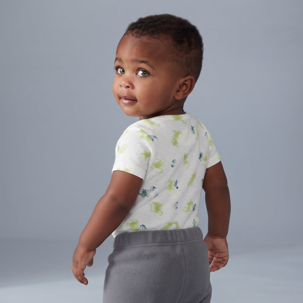 Bebé con body blanco estampado de dragones verdes y pantalón gris de EmpiBy, vista trasera sobre fondo neutro.