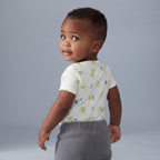 Bebé con body blanco estampado de dragones verdes y pantalón gris de EmpiBy, vista trasera sobre fondo neutro.