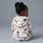 Bebé niña de espaldas vistiendo conjunto EmpiBy de chaqueta y pantalón con estampado floral azul sobre fondo gris.