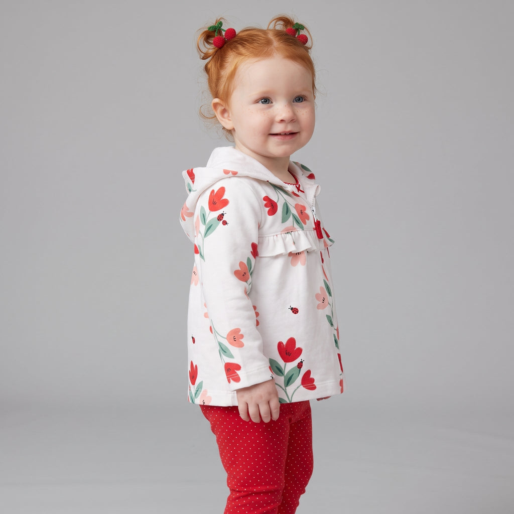 Niña pequeña con conjunto EmpiBy de chaqueta blanca con flores y mariquitas, body y leggings rojos de lunares